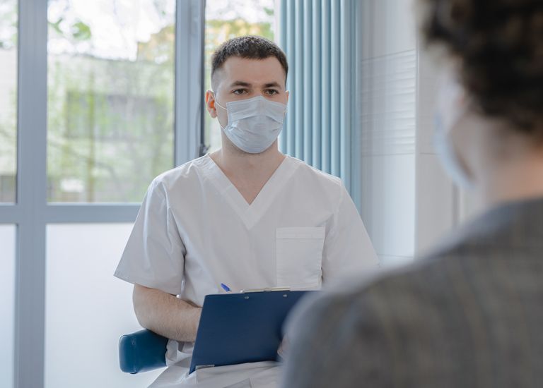 A masked clinician takes notes during a patient visit